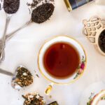 A selection of loose leaf teas along with a cup of tea and a teapot